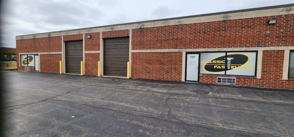 Outside photo of Classic Fasteners main headquarters with 2 garage doors and 2 logos on the window. The building is Chicago common red brick.